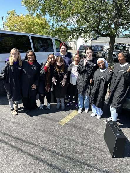 A group of students wearing black jackets standing outside and smiling.