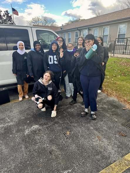 A group of students wearing black and navy blue jackets standing outside and smiling.