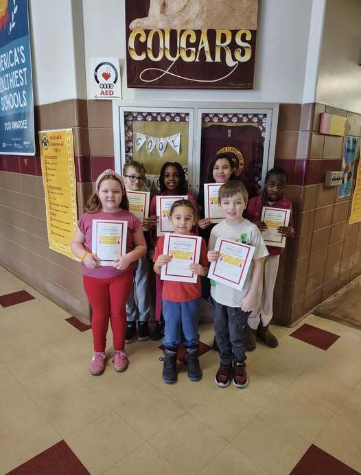 Students standing in a hall and holding up their award.