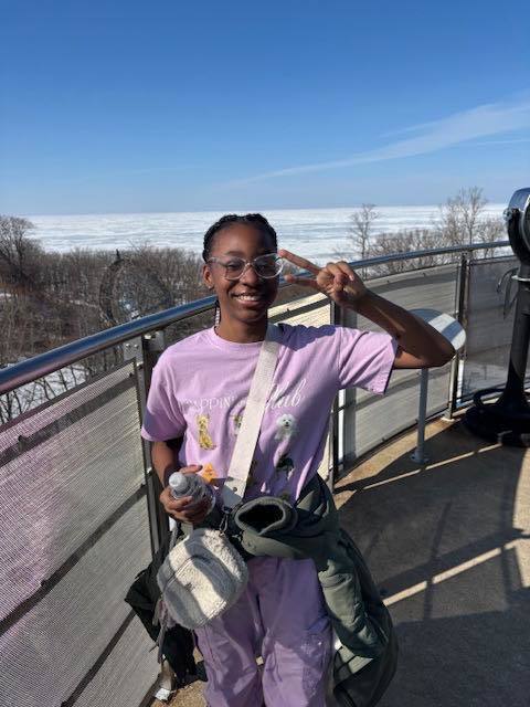A young girl in a purple outfit standing outside  with a frozen lake behind them. 