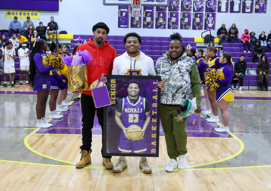 A young man holding up a poster of himself and his family next to him also holding hist poster.