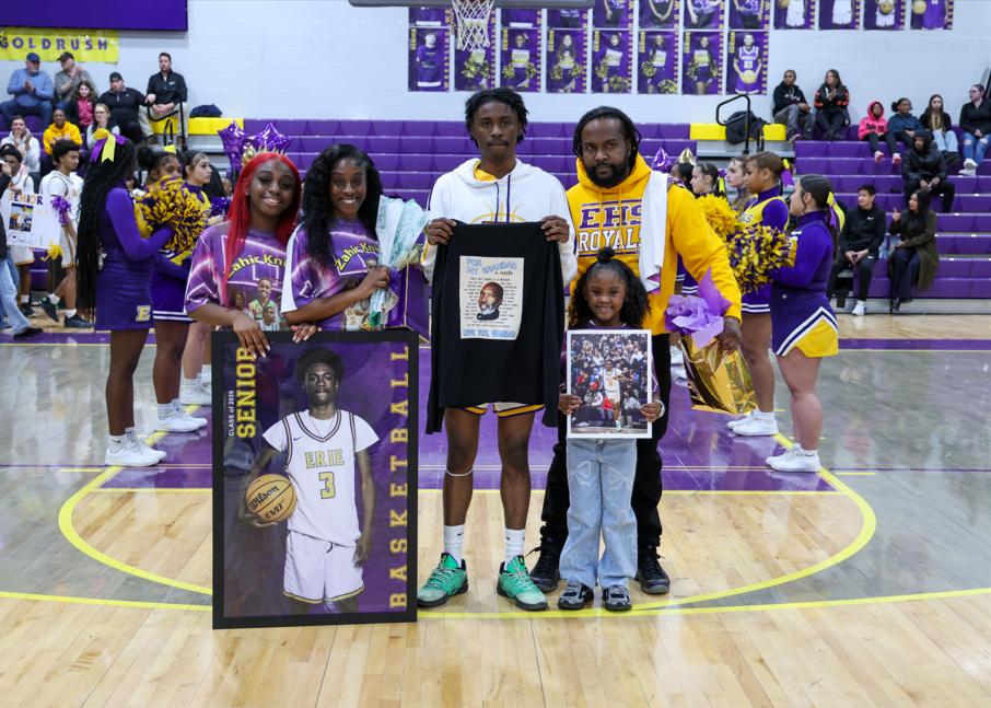 A young man holding up a poster of himself and his family next to him also holding hist poster.
