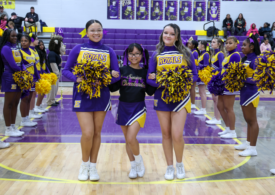 Two chearleaders standing next to a cheerleader who is wearing a senior chearleader hoodie.