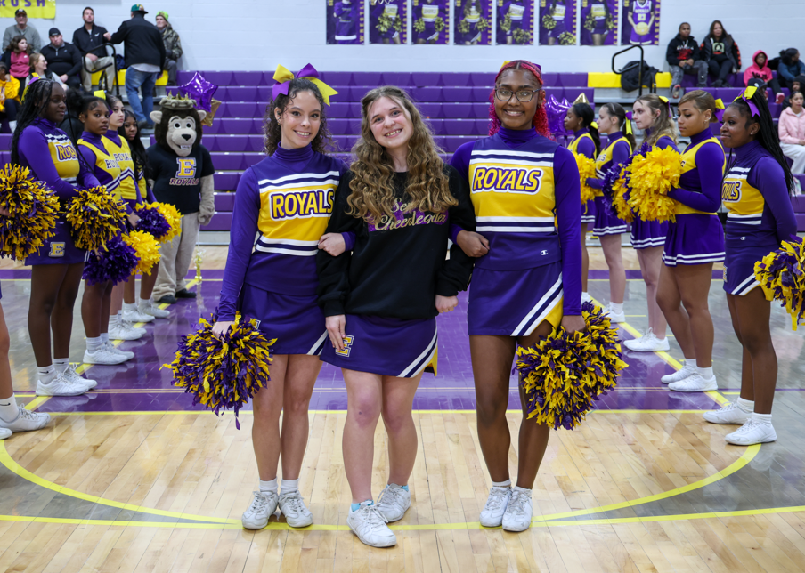 Two chearleaders standing next to a cheerleader who is wearing a senior chearleader hoodie.