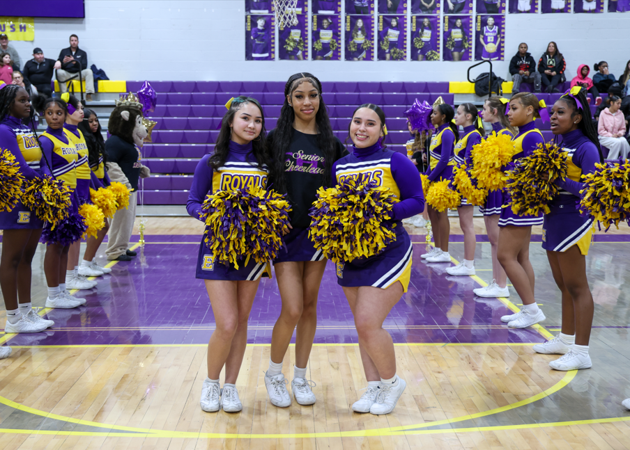 Two chearleaders standing next to a cheerleader who is wearing a senior chearleader hoodie.