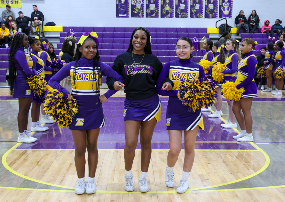 Two chearleaders standing next to a cheerleader who is wearing a senior chearleader hoodie.