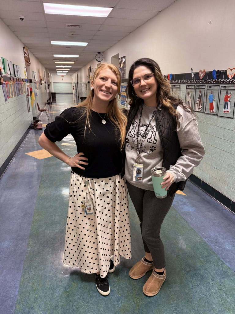 Two women standing in the hall of a school smiling. 