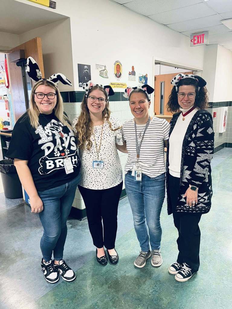 Four women standing in a school hall with Dalmatian ears added on their head.