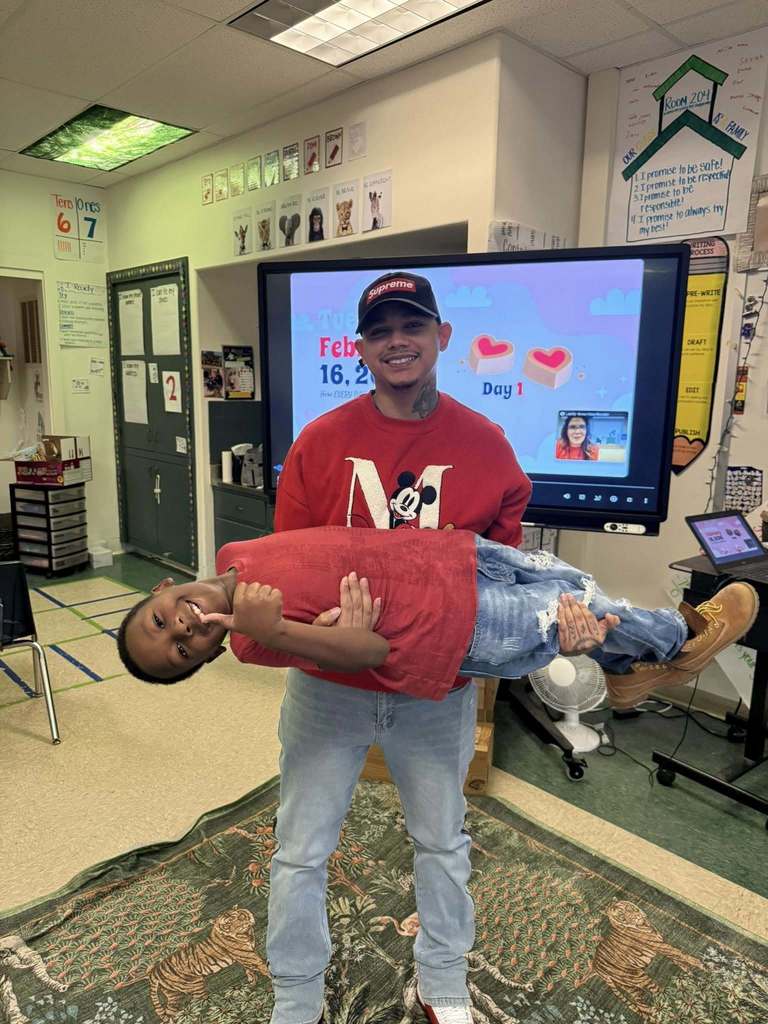 Teacher in a red shirt holding a student smiling in a red shirt.