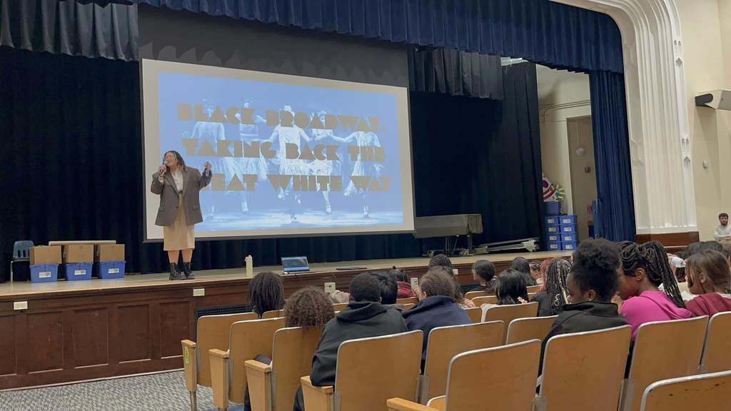 Students in the auditorium watching a young women talk.