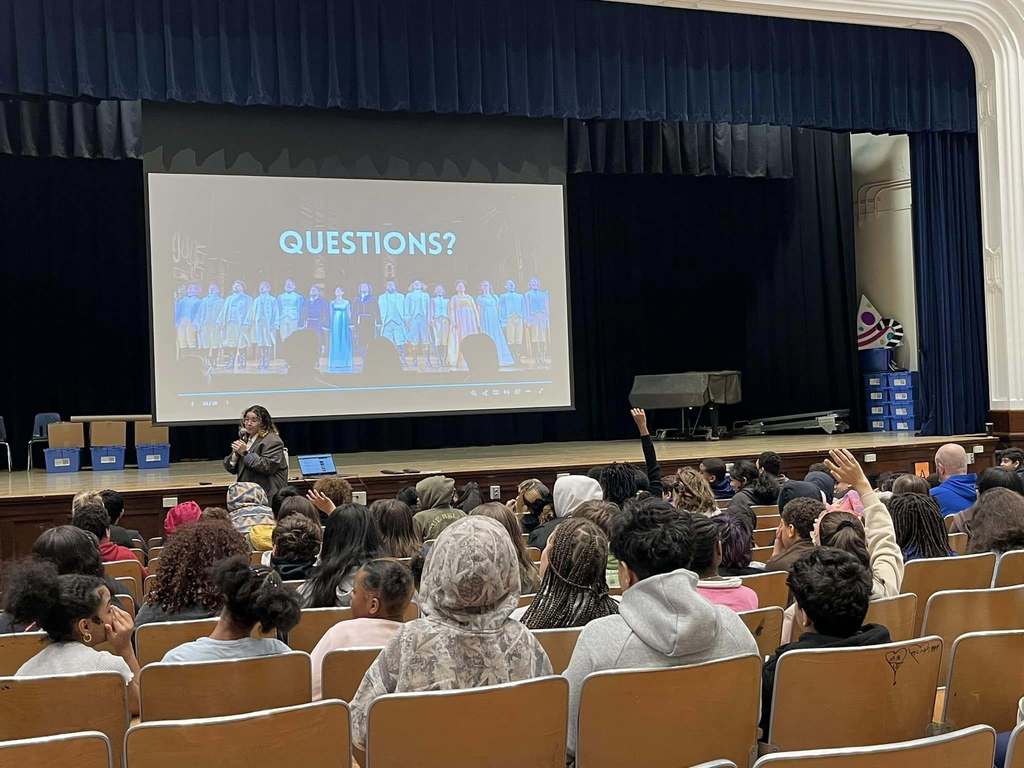 Students in the auditorium watching a young women talk.