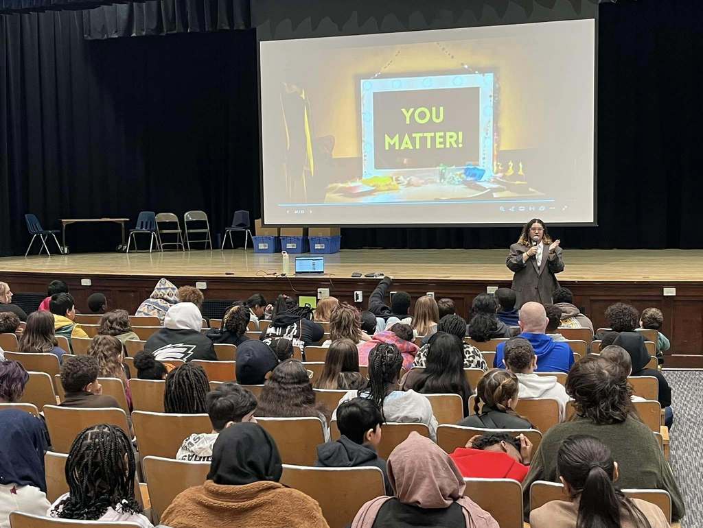 Students in the auditorium watching a young women talk.