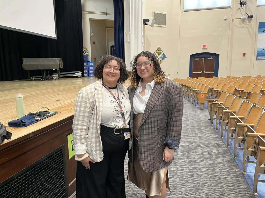 Two young women standing in an auditorium and smiling. 