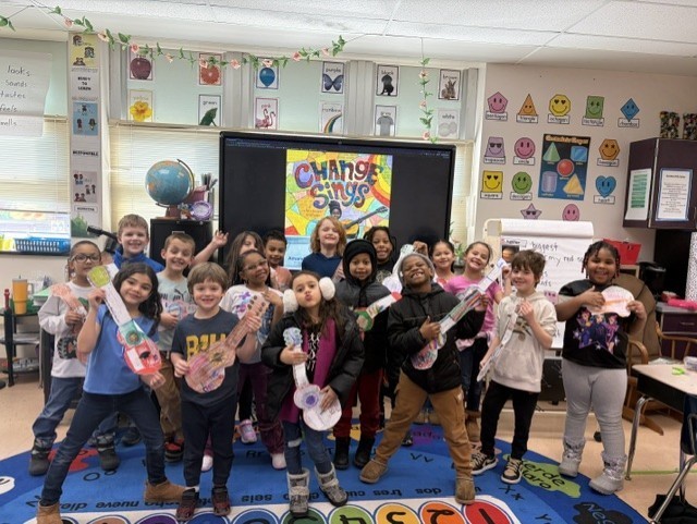 Kids holding paper instruments they colored in a classroom.