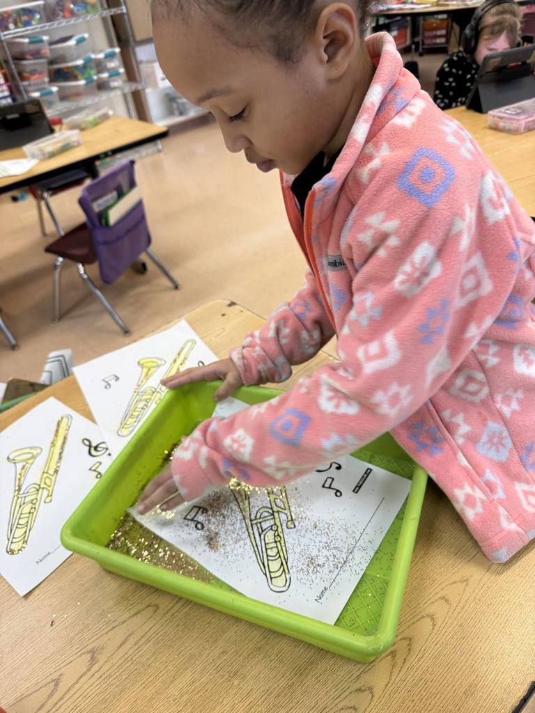 Kids putting glitter on a paper with a colored trombone on it.