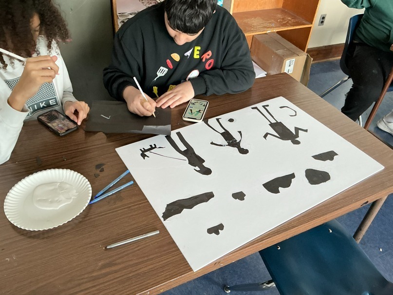 Student making art on white paper using silhouette cut-outs. 