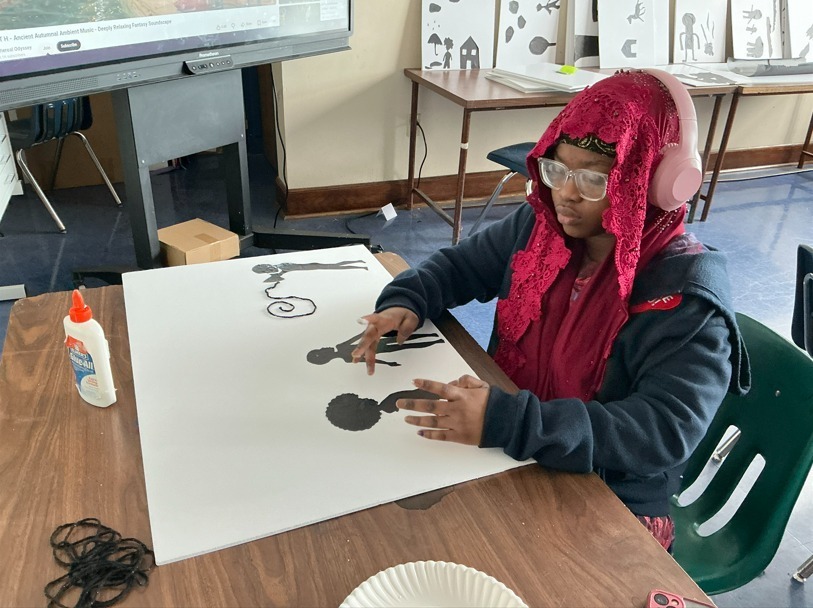 Student making art on white paper using silhouette cut-outs. 