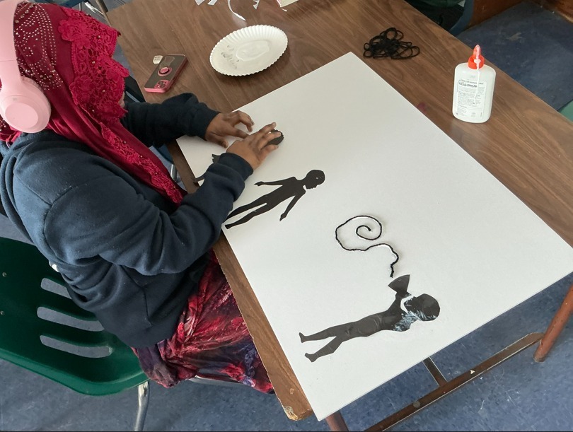 Student making art on white paper using silhouette cut-outs. 