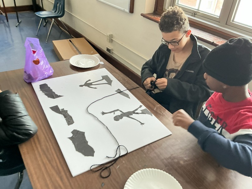 Student making art on white paper using silhouette cut-outs. 