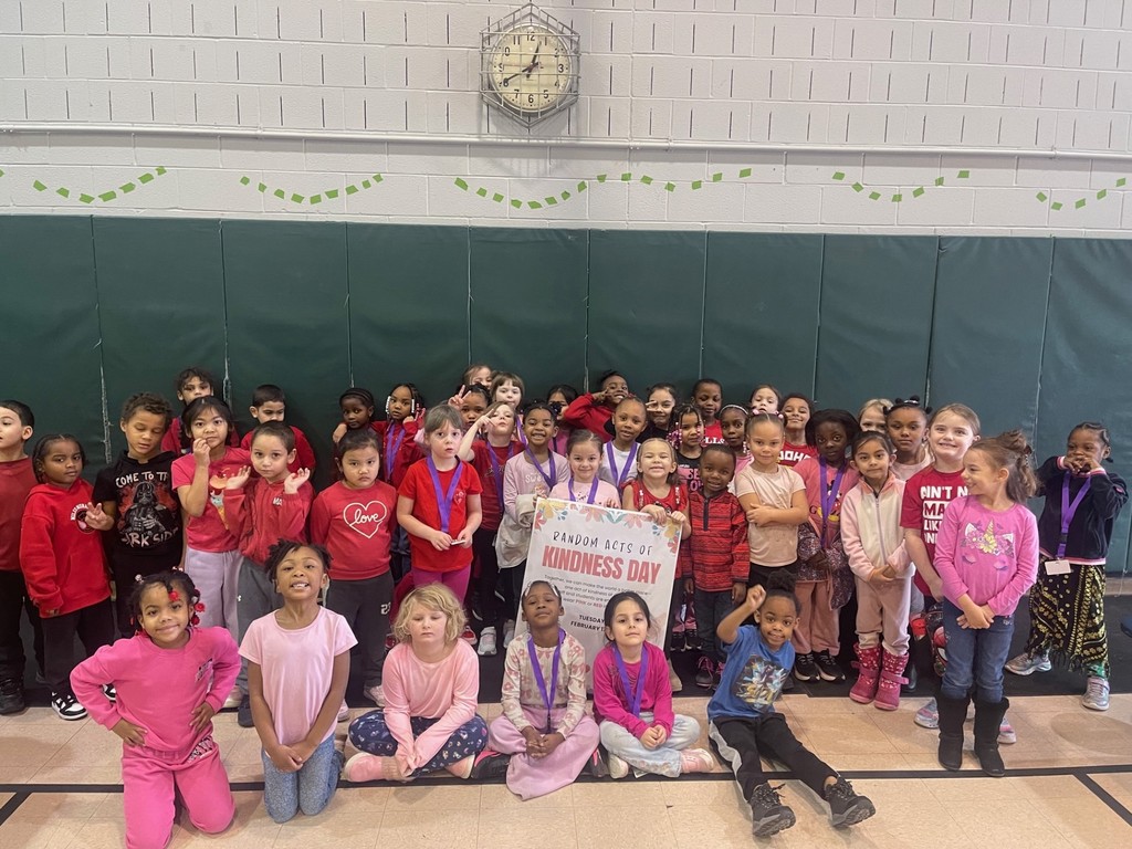 Students wearing red and pink for Random Acts of Kindness Day as they hold the poster for the day. 