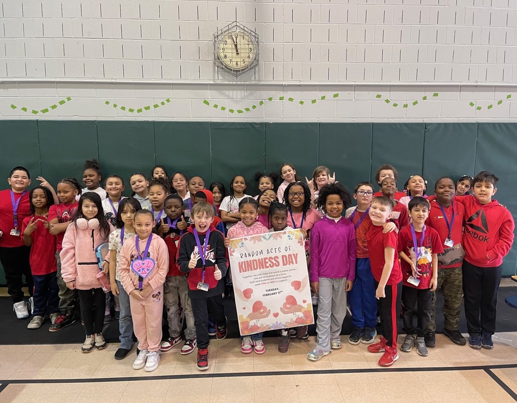 Students wearing red and pink for Random Acts of Kindness Day as they hold the poster for the day. 