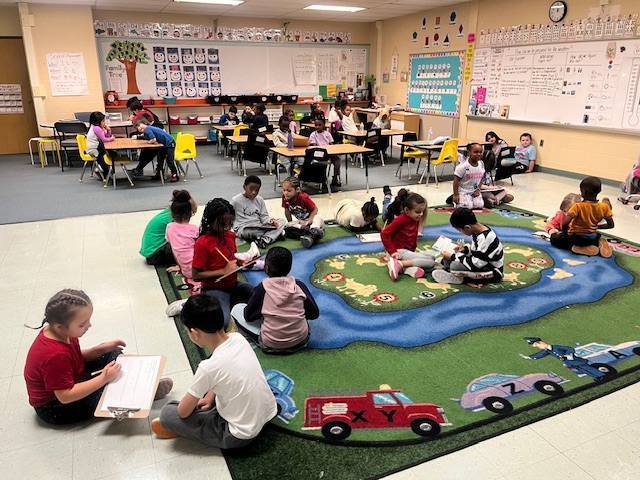 Students sitting in pairs on the floor of a classroom and working on an assignment.