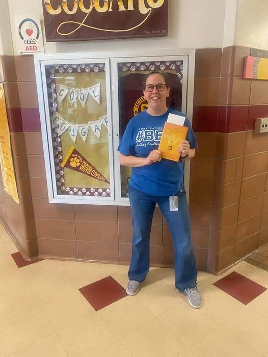 A women wearing a blue shirt that says hastag BET and is standing in the hall smiling.