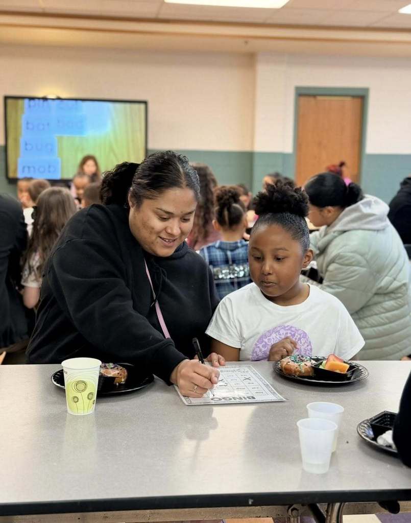 A student with their family eating breakfast and playing bingo at school.