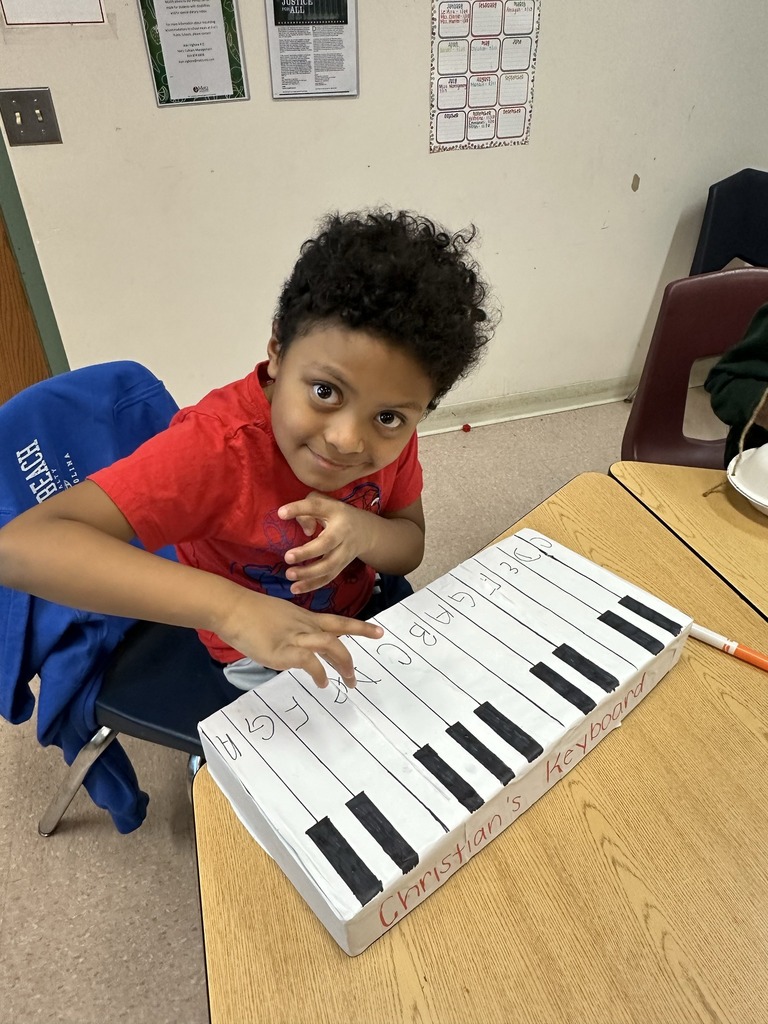 Student holding acting like he is playing a piano he crafted from items in the classroom.