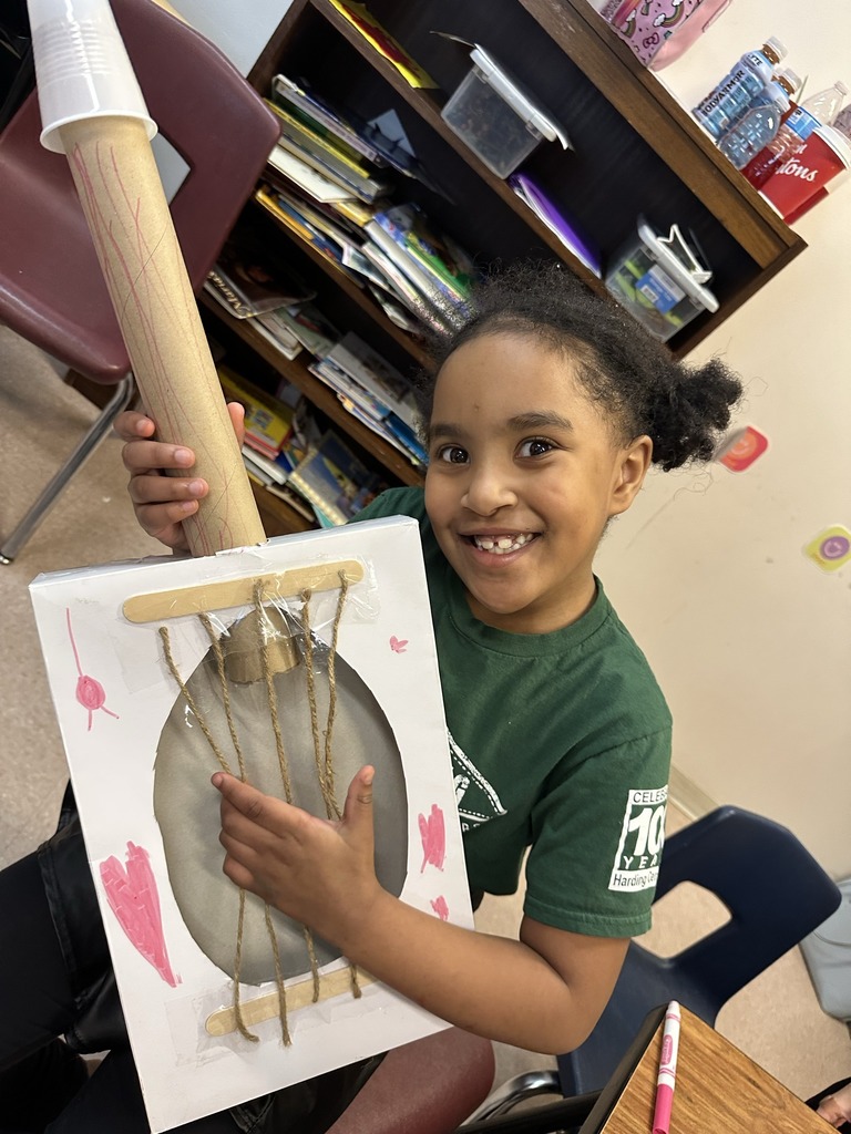 Student holding a guitar they crafted from items in the classroom.