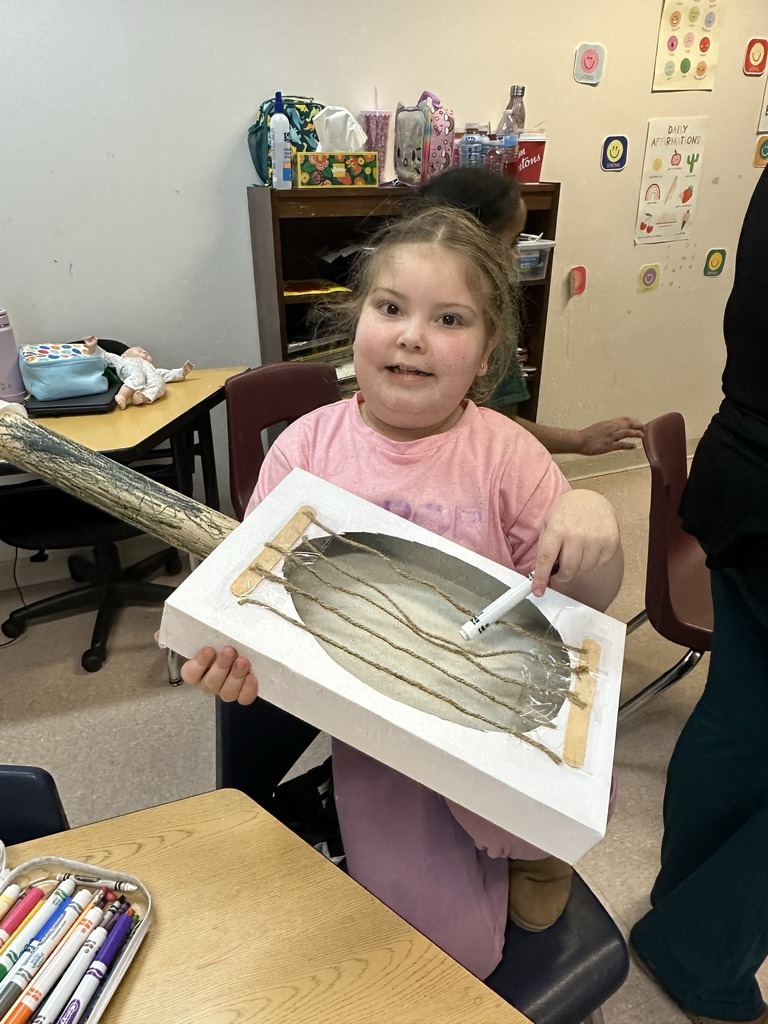 Student holding a guitar they crafted from items in the classroom.