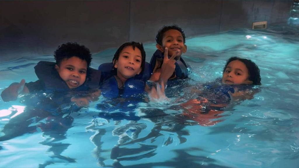 Kids in a pool wearing life jackets.
