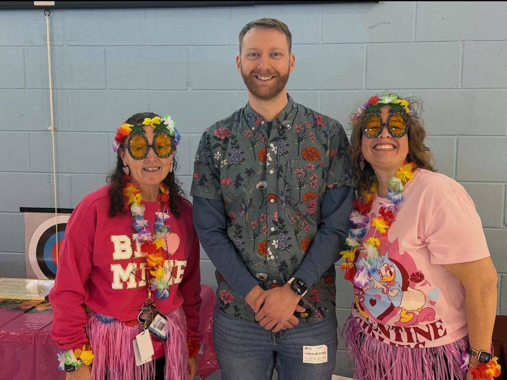 Two women dressed in Luau attire and are standing next to  David Gorman.