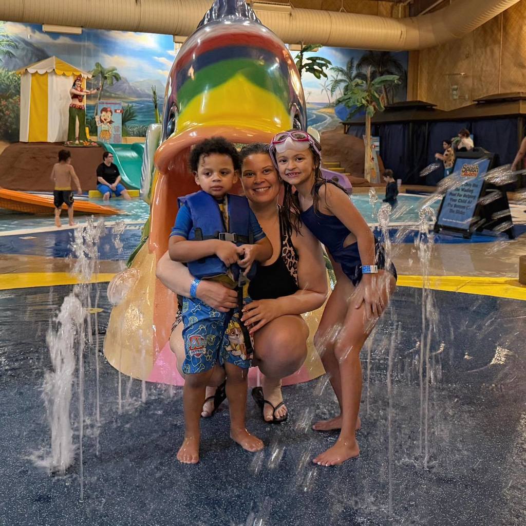 Kids smiling next to an adult at a water park. 