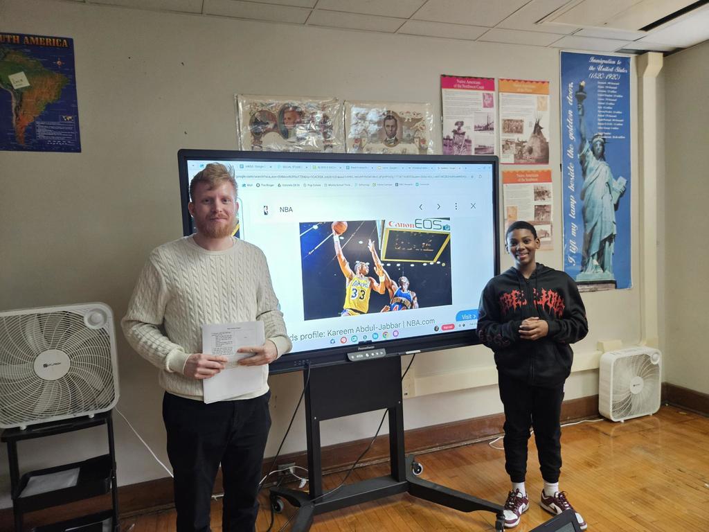 Two individuals standing in front of a large screen and are ready to present. 