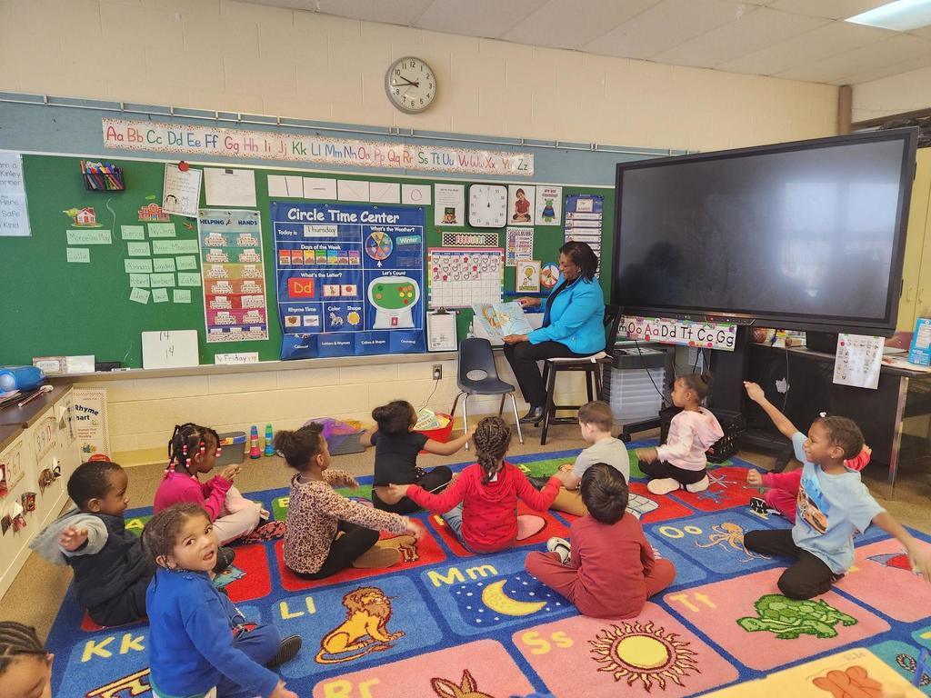 An individual reading to a group of students in a classroom.