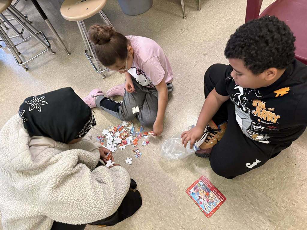 Students are putting together a puzzle on the floor. 