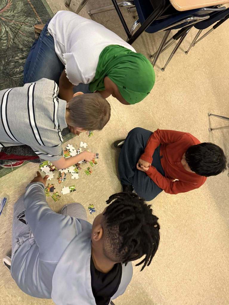 Students are putting together a puzzle on the floor. 