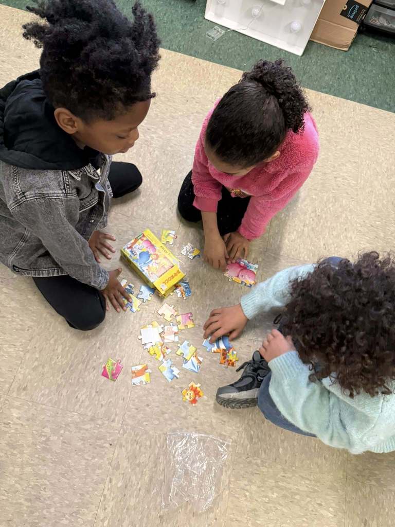 Students are putting together a puzzle on the floor. 