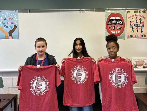 Students holding red shirts with the East Middle School logo on them. 