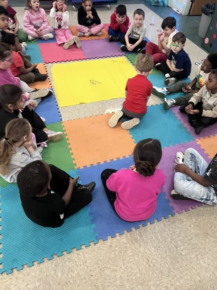 Students waiting to draw and write on a large yellow paper. 