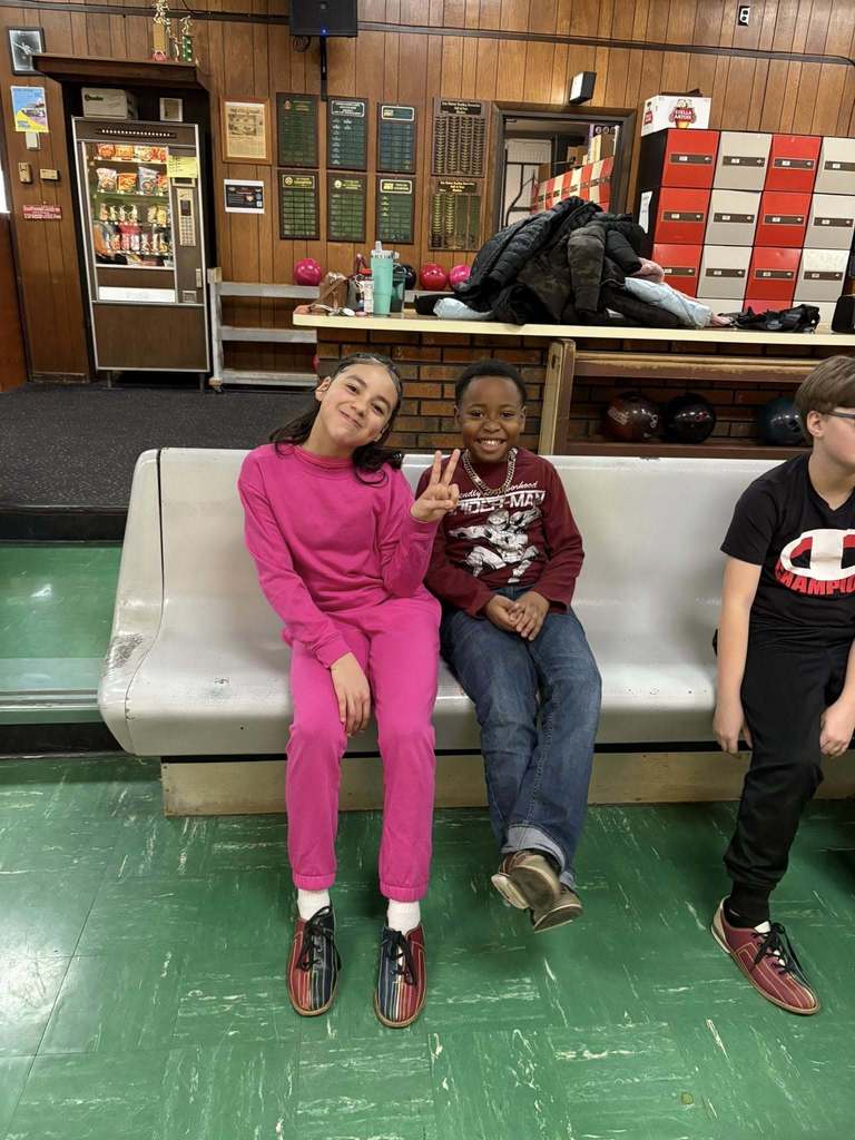 Kids sitting in a bowling ally. 
