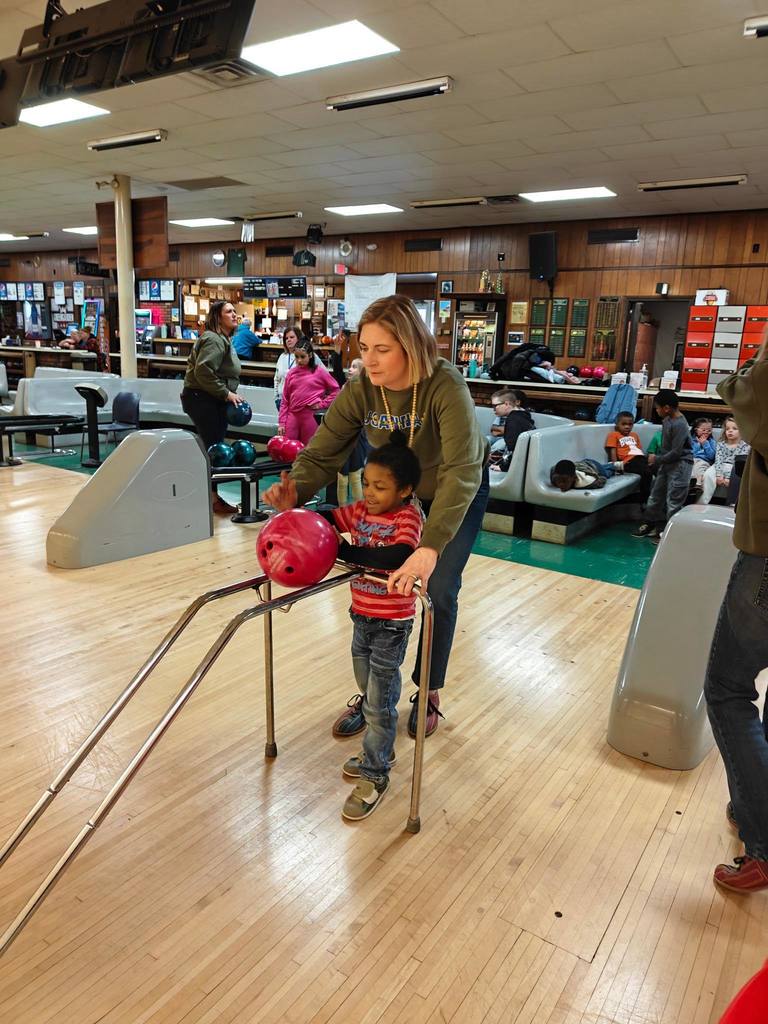A teacher helping a student bowl. 