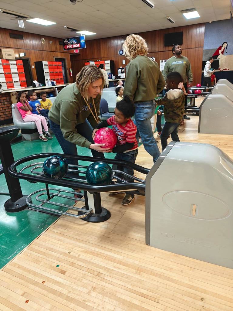 A teacher helping a student cary a bowling ball.