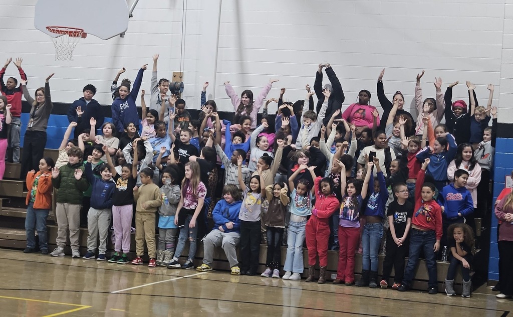 Kids raising their hands and are sitting io bleachers.