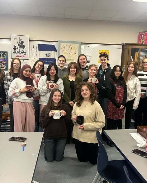 Students in a clasroom smiling and holding mugs.