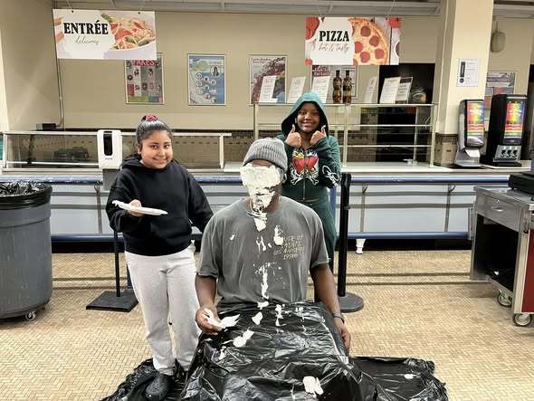 Students pied a teacher who is sitting in a chair.