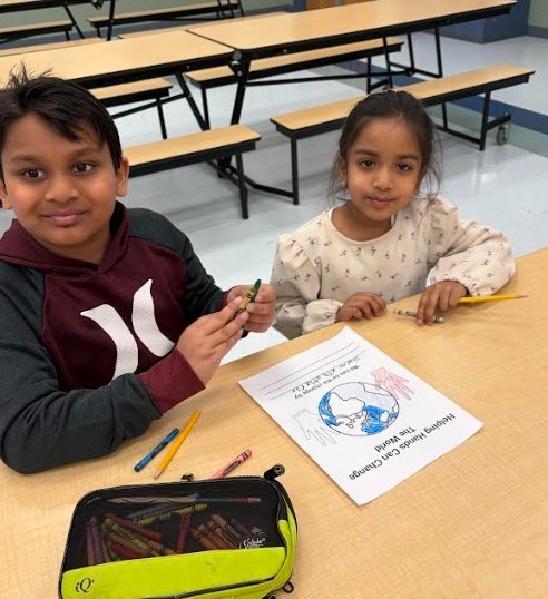 Two children, a boy and a girl, sit at a table with coloring tools and paper.