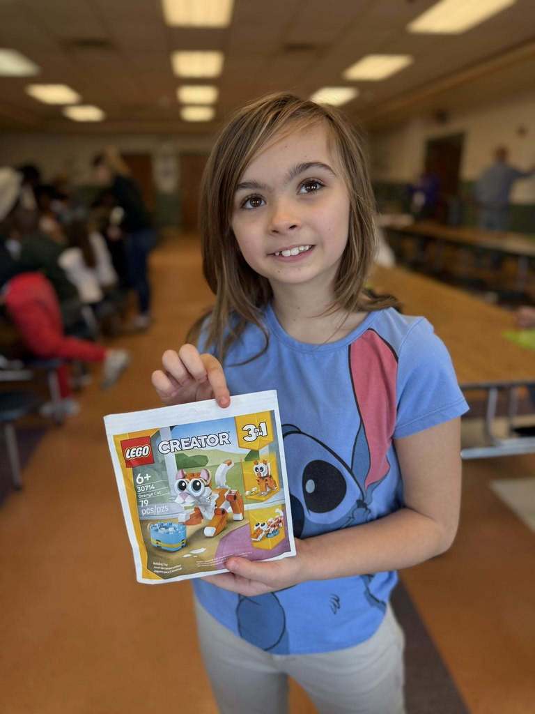 A kid holding a lego set they won. 