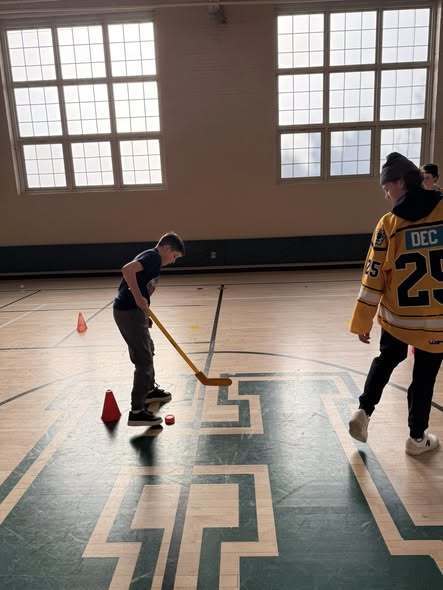 Kids playing hocky in a school gym with Erie Otters Hocky Players. 